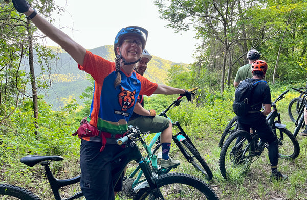 a female cyclist spreads her arms in joy with a group of mountain bikers on a trail