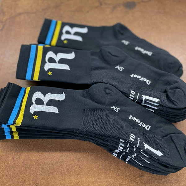 custom DeFeet black cycling socks with a colorful diamond pattern on legs in the air