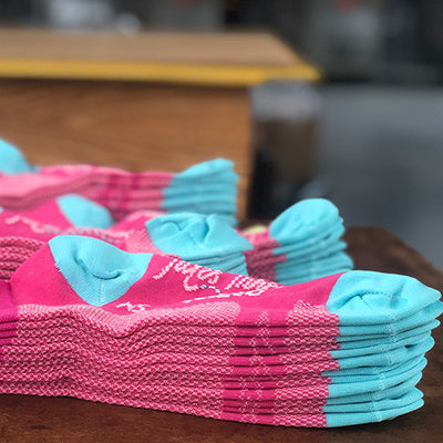 Custom DeFeet cycling socks in hot pink and blue stacked on a table