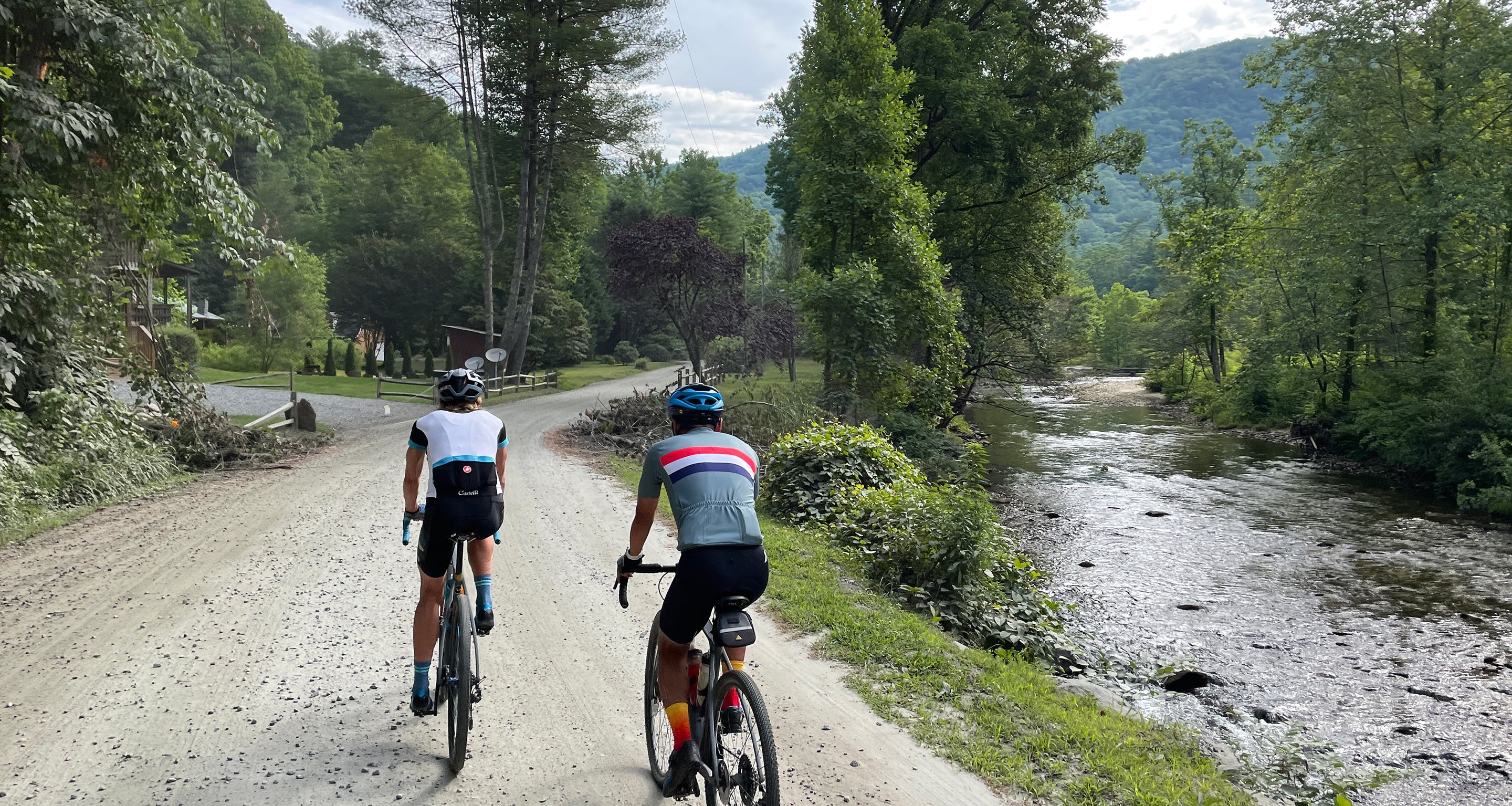 two cyclists wearing DeFeet cycling socks ride on a gravel road beside a river