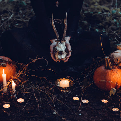 pagan spell ritual, witch kneeling on the ground holding animal skull and surrounded by a circle of candles