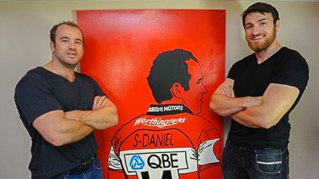Shane Monahan and James Simpson Daniel pose in front of a painting of James Simpson Daniel
