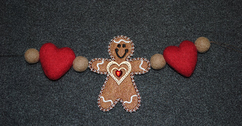 Picture of free-standing machine embroidered gingerbread man with latte felted heart and ball attached to both arms.