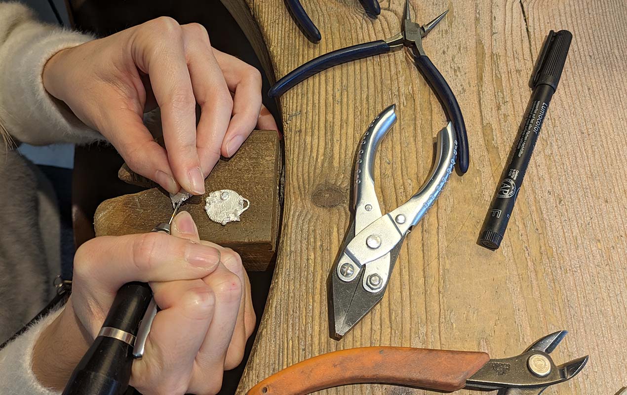 A worktop with tools and a person’s hands as they create an intricate design on jewellery.