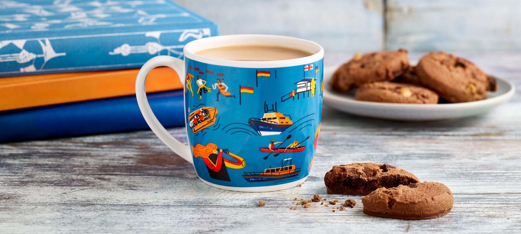 Close up shot of a mug with a colourful Jonty Storey lifeboat patten on it, next to a broken cookie