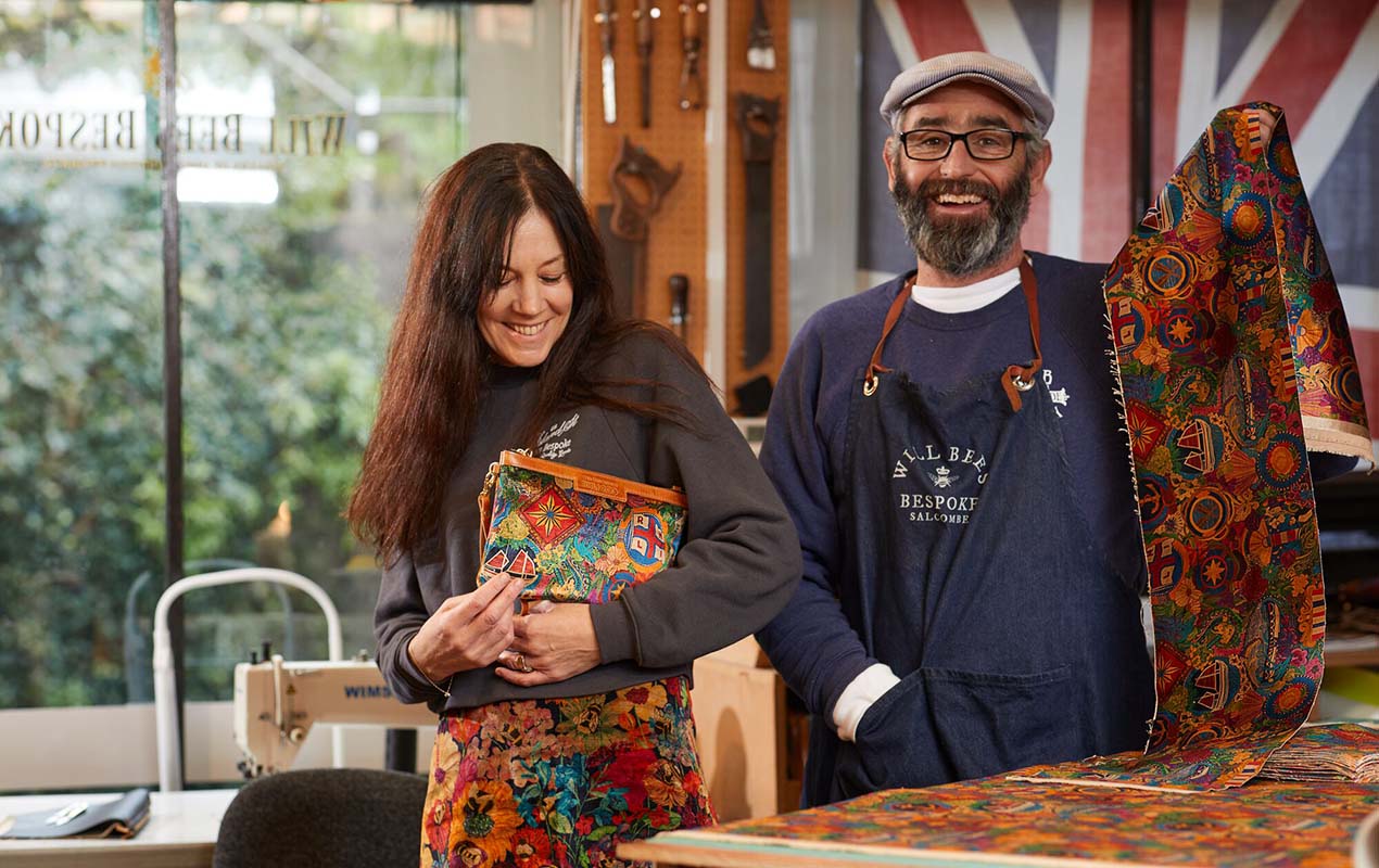 Designer Emma Mawston holds a beautiful clutch bag featuring her exclusive RNLI design, and is stood next to Will Bees who is holding the velvet fabric.