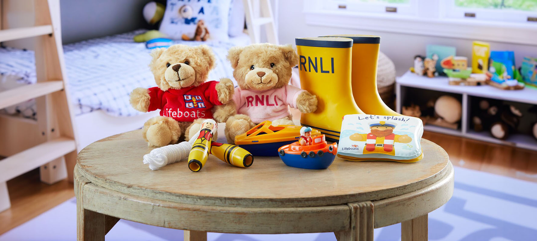 A wooden table with some kids’ toys on it, including two RNLI teddy bears, a pair of RNLI welly boots, and beach games. The table is in a child’s room and there is a bunkbed and toy storage in the background.