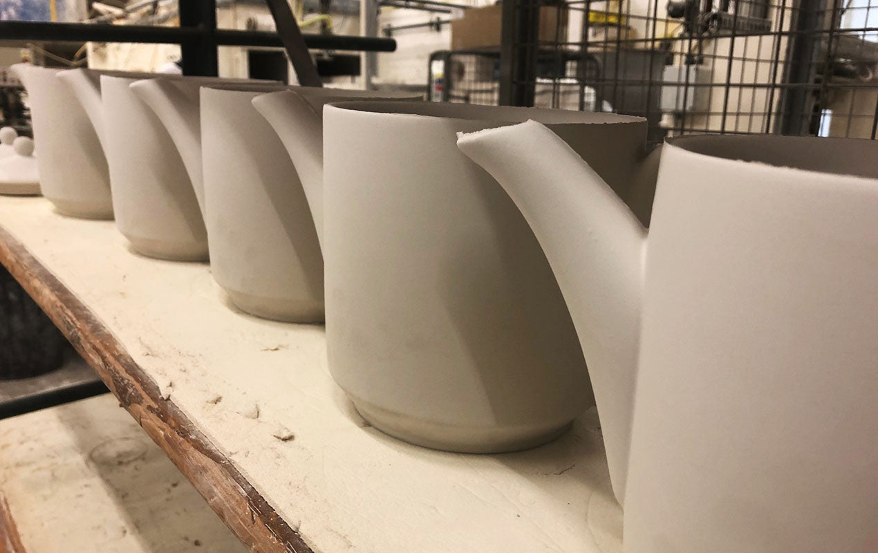 A line of unpainted teapots on a shelf in a workshop.