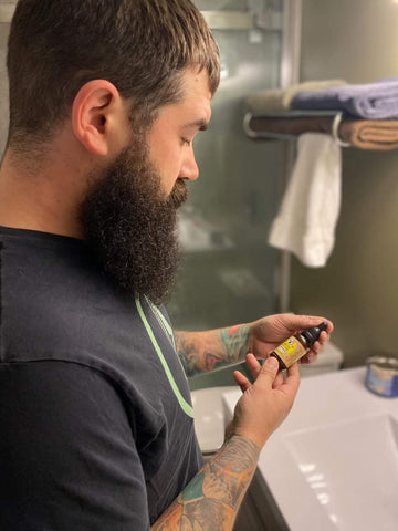 A bearded man looking at a bottle of beard oil