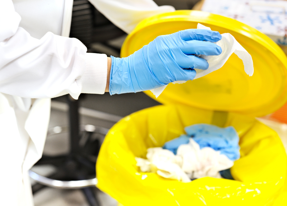 a person wearing blue disposable gloves is throwing something into a yellow hazardous waste bin with disposable gloves and other medical supplies