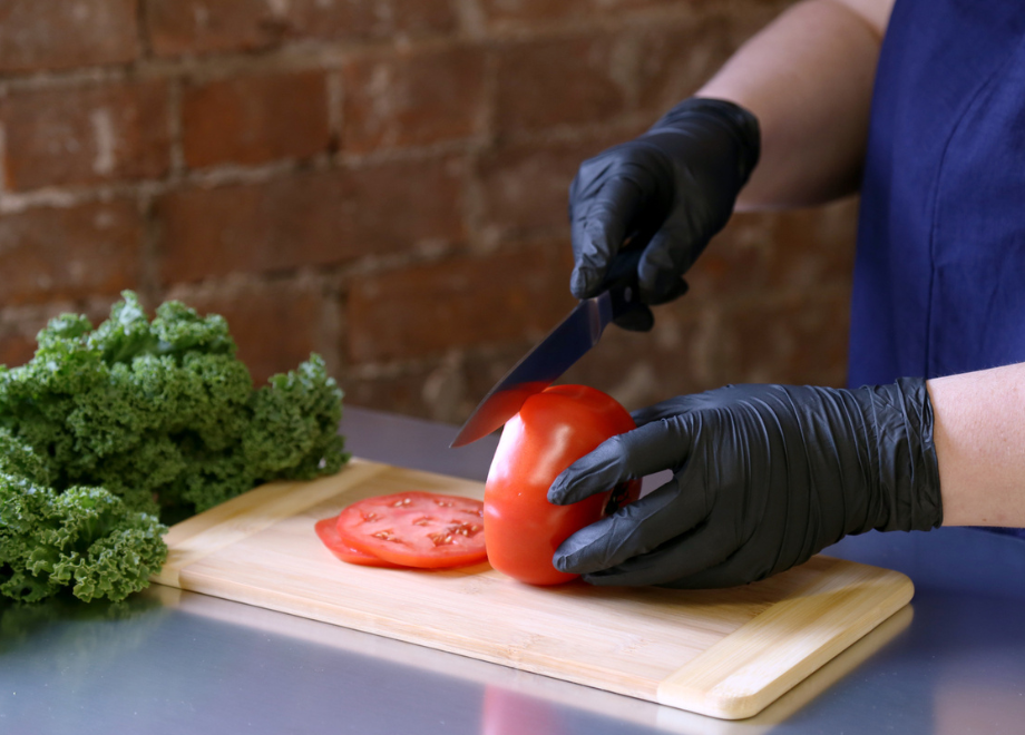 tomato being sliced with knife by gloved hand