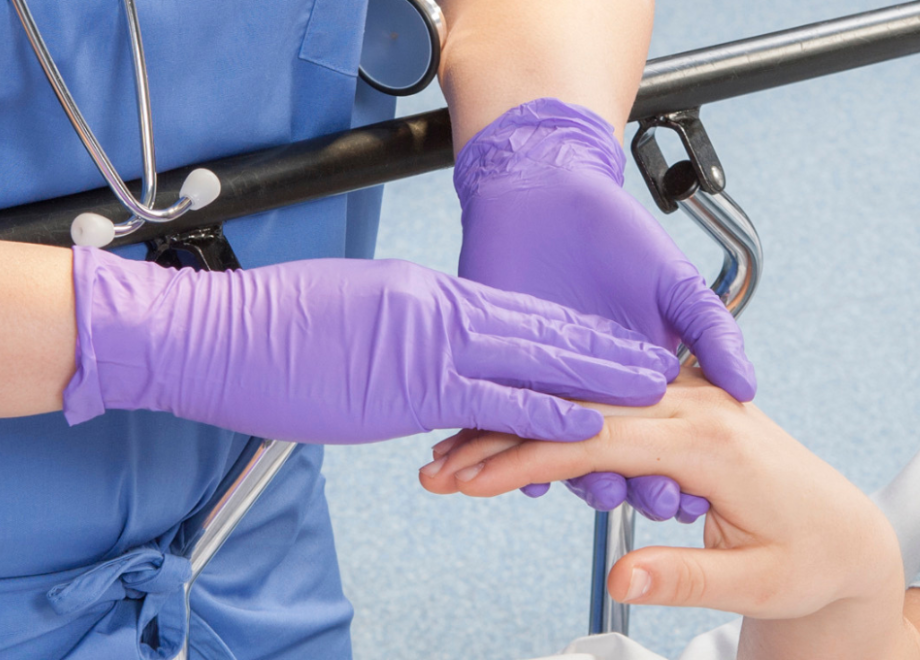 nurse caring for patient while wearing purple nitrile grape grip disposable gloves