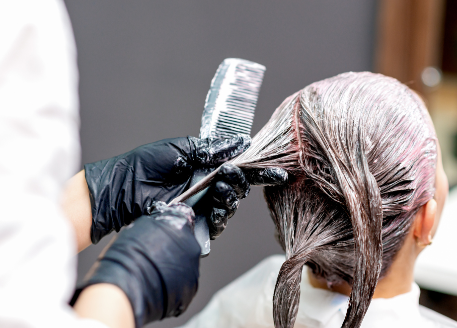 A gloved hand applies hair dye to another person's hair