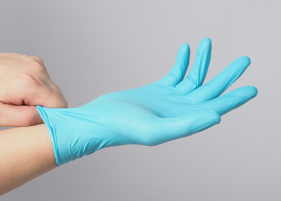 Blue latex glove being stretched over a person's right hand. Grey background.