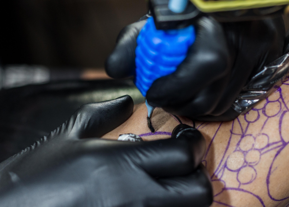A person wearing black disposable nitrile gloves is tattooing an undetermined body part on another person