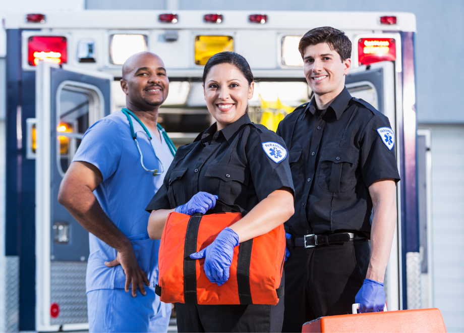 Two first responders in nitrile gloves next to a nurse in front of an ambulance