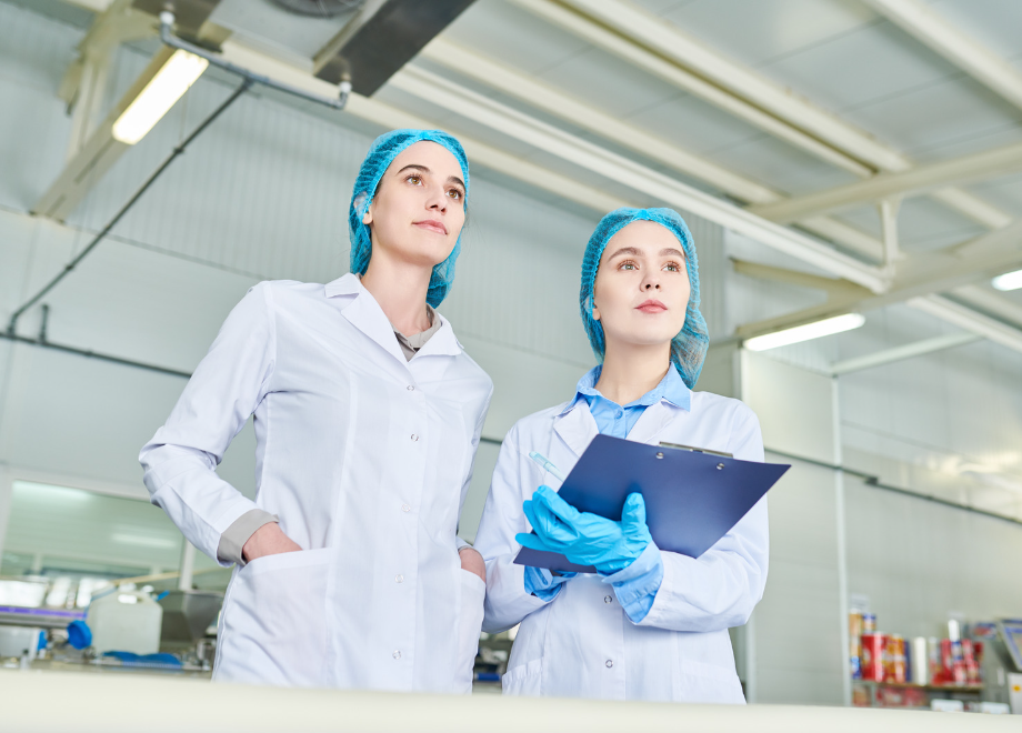People in a food manufacturing facility wearing disposable gloves and holding a clipboard