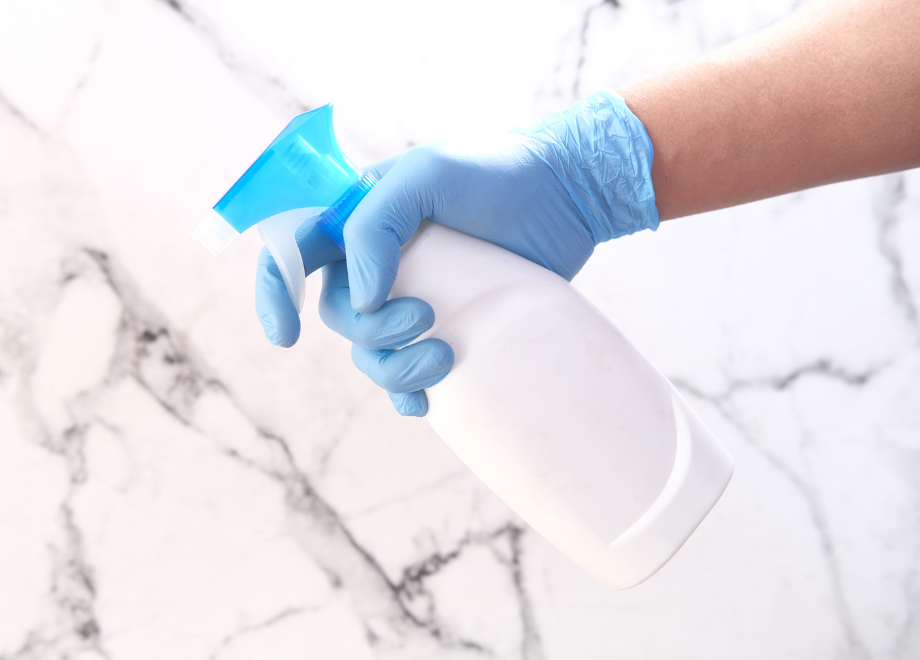 person wearing blue nitrile gloves and using a spray bottle