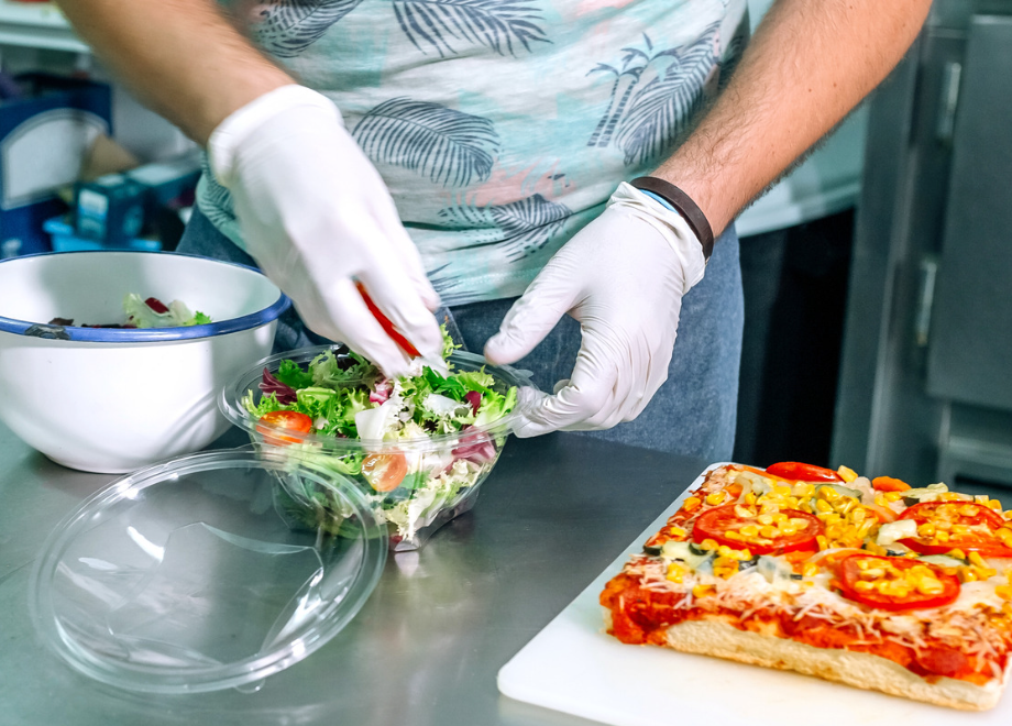 person wearing disposable gloves and prepping a salad