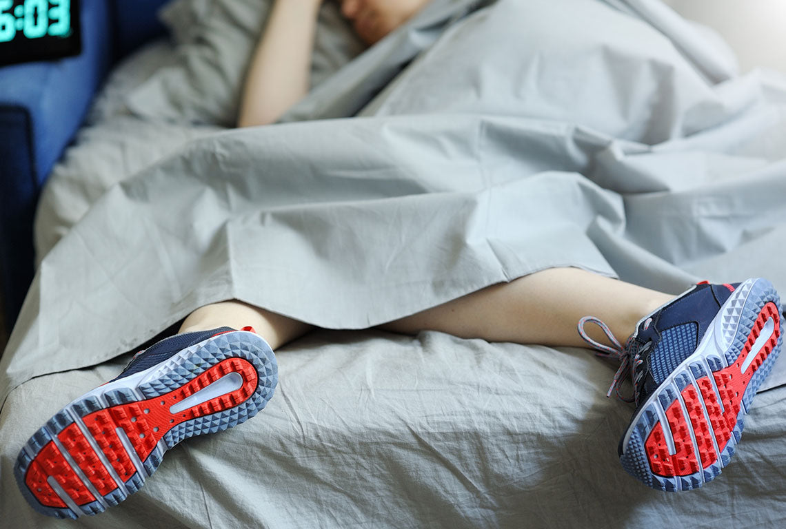 Person sleeping with running shoes in bed