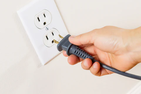 hand plugging a cord into an electrical outlet