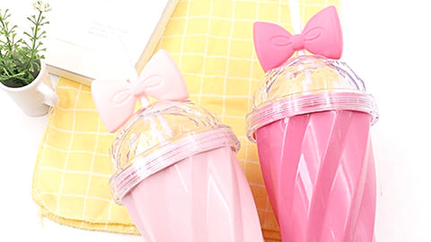 Second Belle bow cup image shows the blush pink and fuchsia options with their transparent spill proof covers and signature bowtie sippy straws. White counter with yellow dishcloth and a some green seasoning herbs tell a story: these cups are must have items for new home owners with kids. They look durable and can limit a spill.