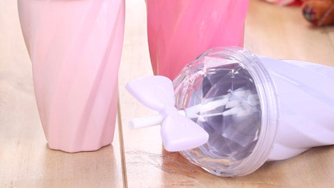 Belle bow cup image shows 3 cup colors: blush pink, fuchsia & lavender, on a hardwood floor. The lavender cup is on its side, showing off the signature bowtie sippy straw with transparent spill proof lid.