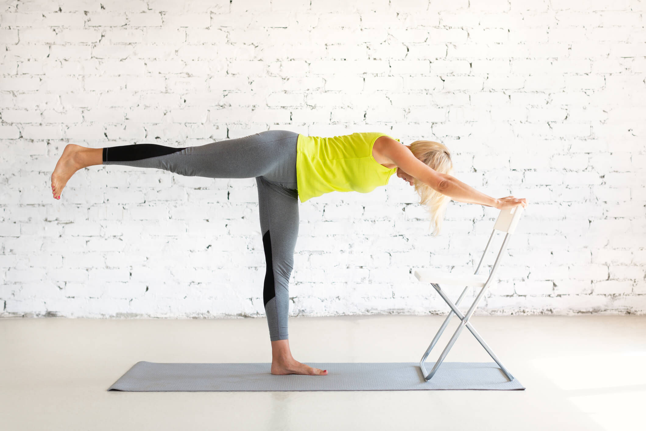 older lady doing yoga half moon pose using chair as prop for support