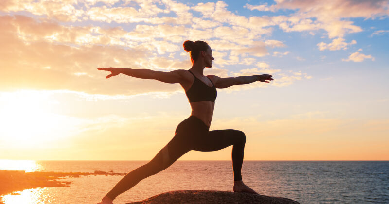 Woman practicing warrior pose in front of sunset