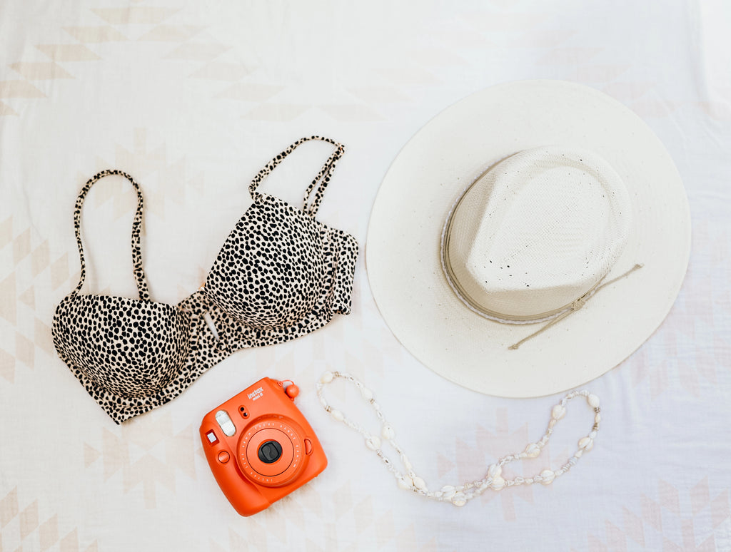 image of a leopard print bikini top, an orange polaroid camera and the Corinth Wide Brim Straw Fedora Hat by American Hat Makers