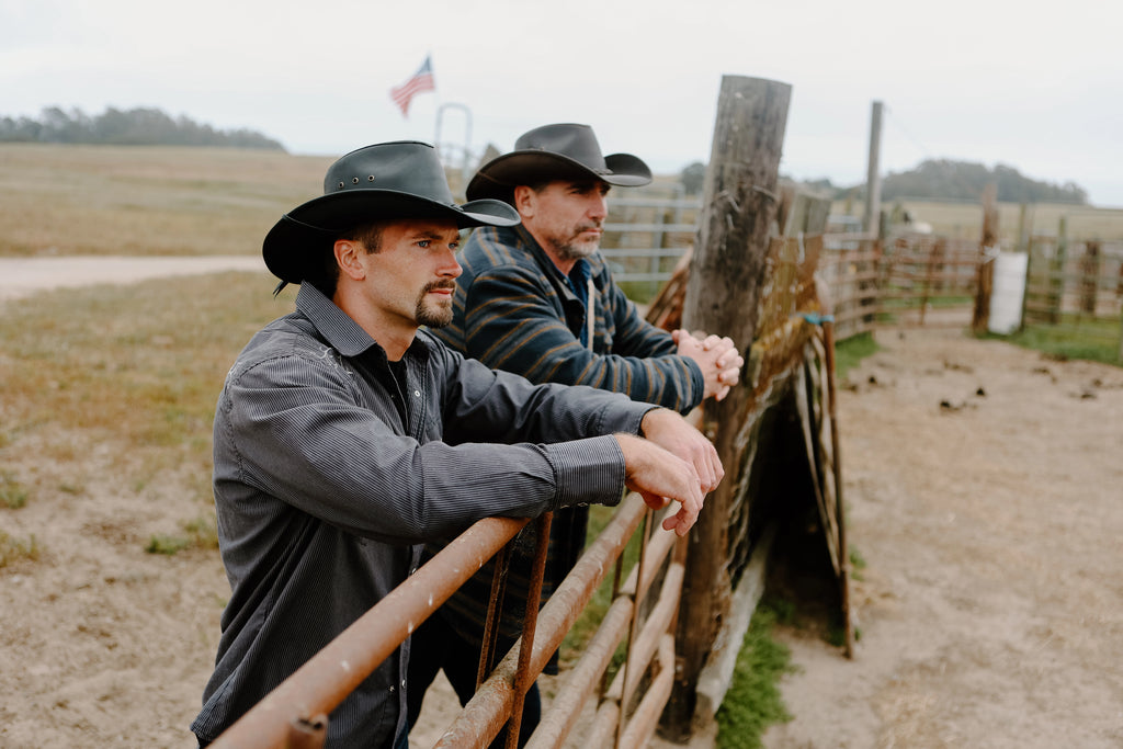 image of two guys, one older, leaning on metal gate around a horse pen