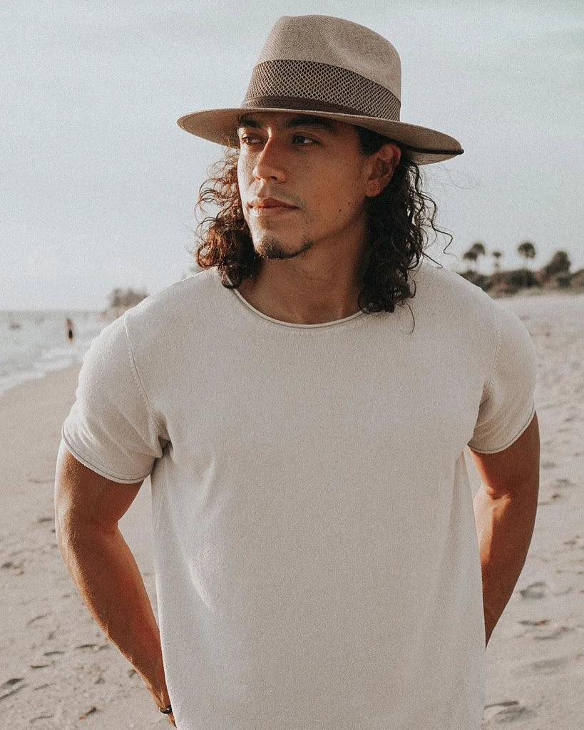image of guy with brown shoulder length wavy hair walking on a beach looking into the distance in a white t-shirt wearing the cream Milan | Men's Straw Fedora Hat by American Hat Makers
