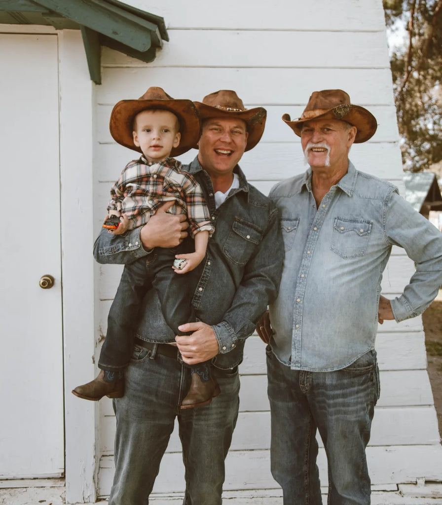 Image of the three generations of men in American Hat Makers. Grandfather, his son and his grandson. They are all wearing blue jeans, long sleeve button-ups and brown cowboy hats by American Hat Makers