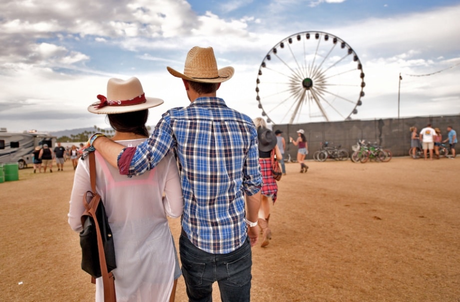 A couple stands in front of a Ferris wheel wearing a felt and a straw cowboy hat