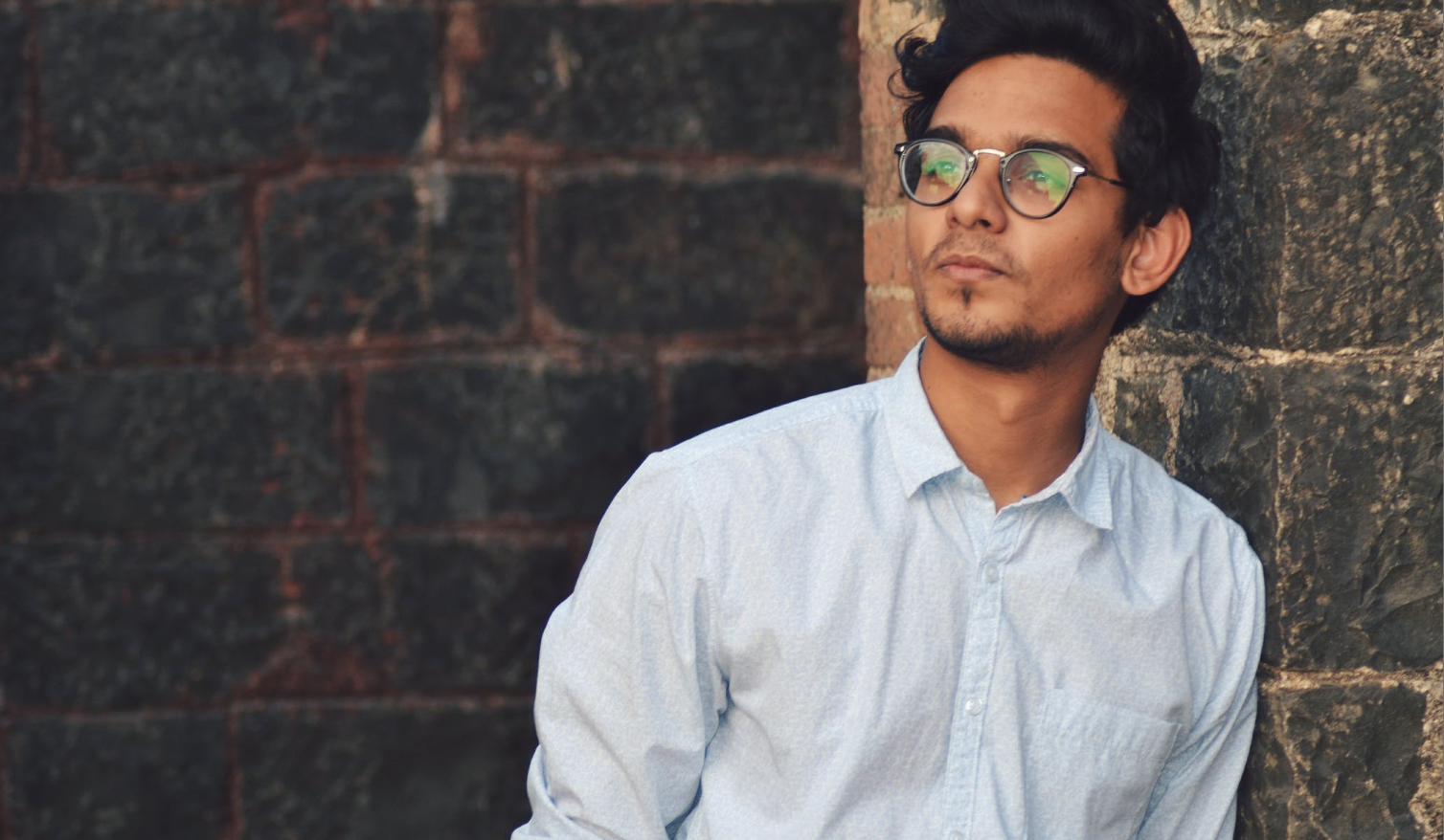 A man wearing eyeglasses is looking pensively at a distance.