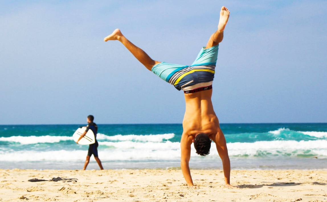 A man is in a handstand position at the beach