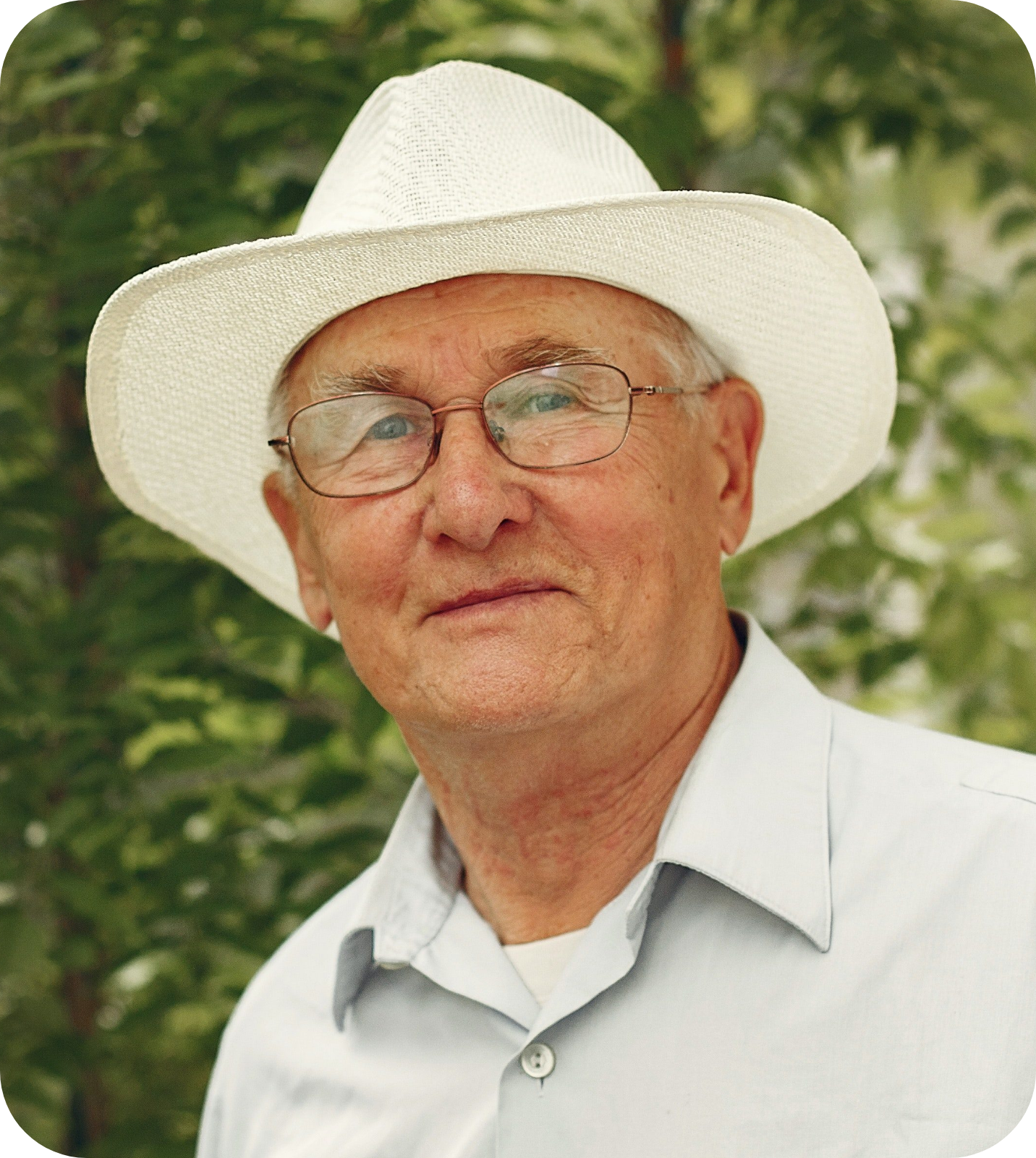 A picture of a senior man with a slightly smiling face, wearing a white hat and eyeglasses.