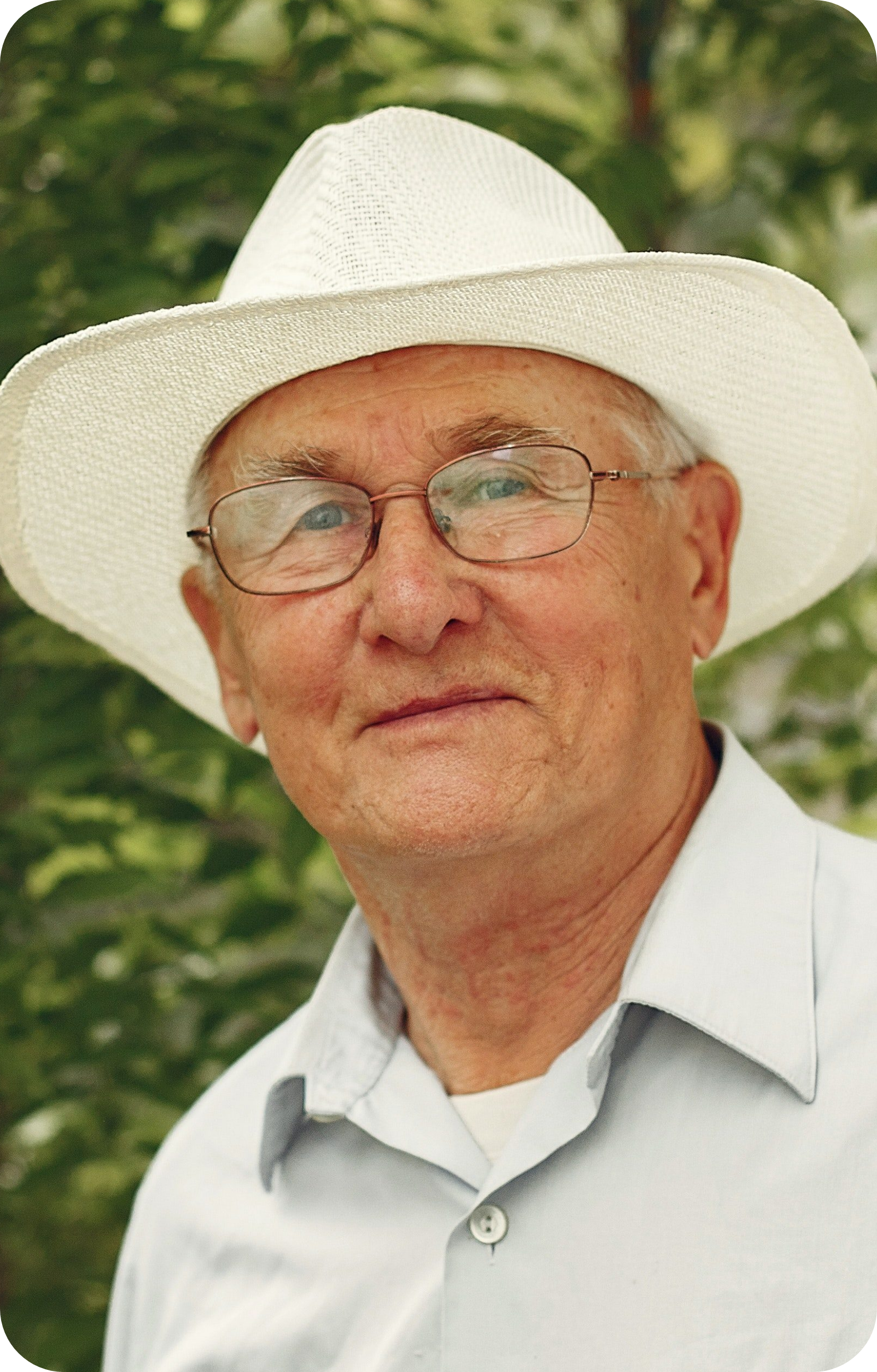 A picture of a senior man with a slightly smiling face, wearing a white hat and eyeglasses.