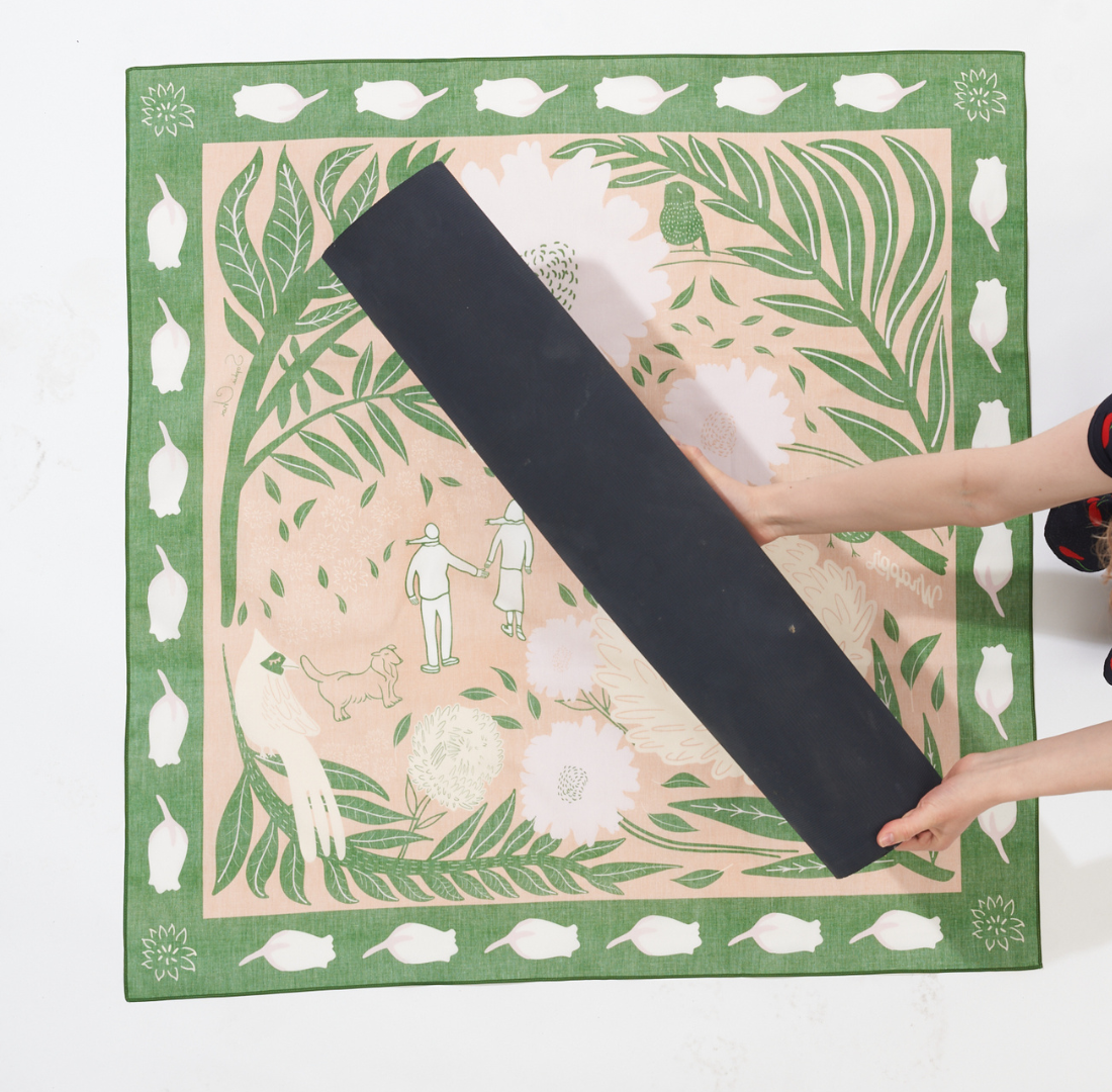 Image of a furoshiki wrap on a flat surface, print side face down and yoga mat placed diagonally at the center
