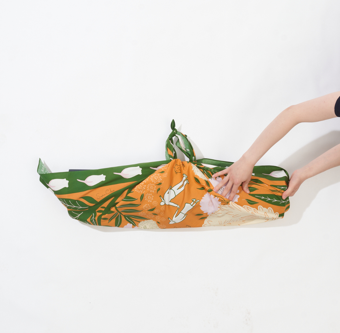 image of someone tucking the fabric in the sides of the furoshiki mat carrier 