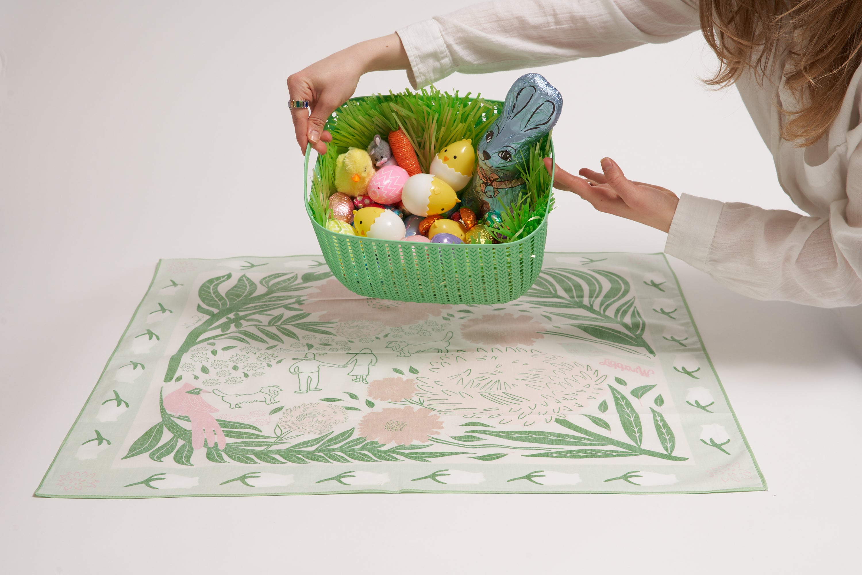 An image of a furoshiki layed flat face down and an easter basket filled with treats hovering over it