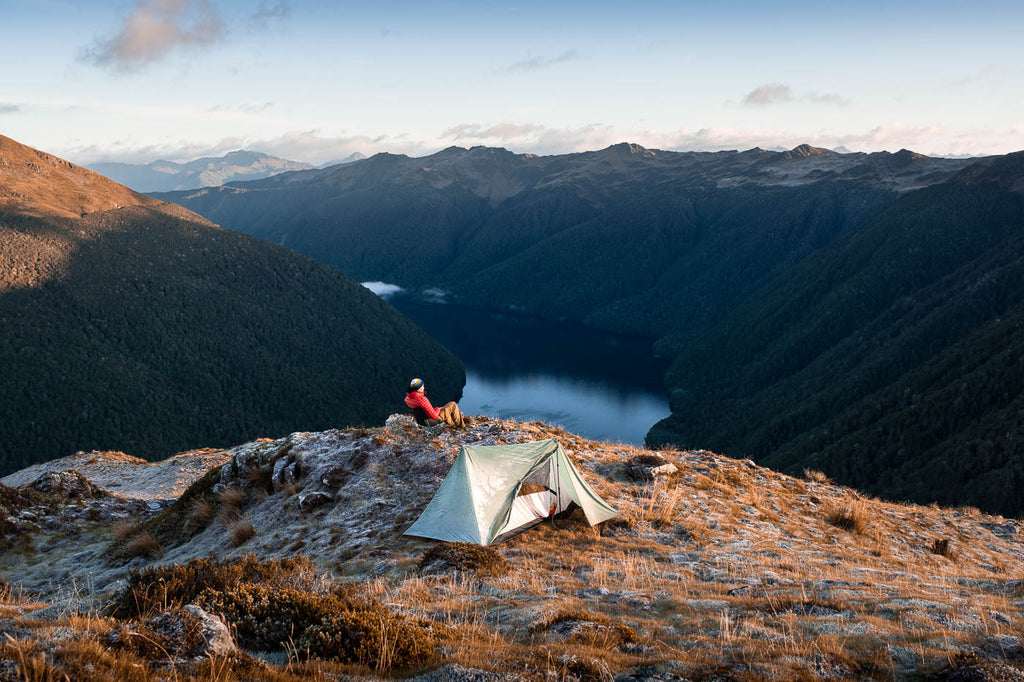 Man sitting by his tent on a mountain overlooking a lake