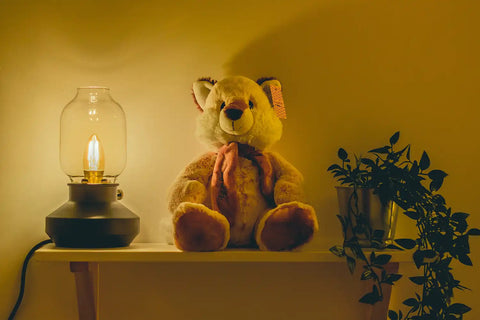 Desk lamp next to a house plant and a teddy bear on a table.