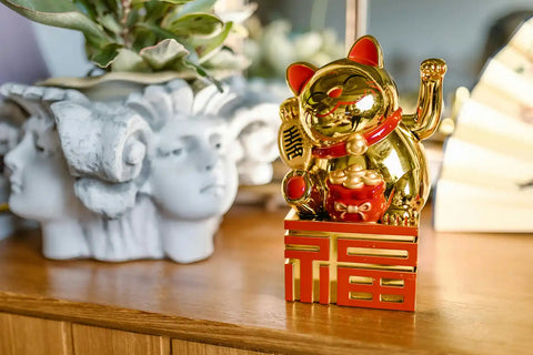 A gold and red lucky cat next to a Roman-style white vase