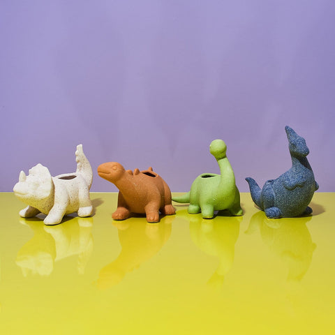 4 styles of Dinosaur Mini Planter Pots from Left to right: white triceratops, clay stegosaurus, green brontosaurus, and blue parasaurolophus