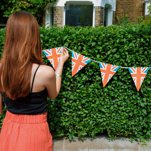 Woman hanging Union Jack Bunting on a hedge preparing for a Coronation street party
