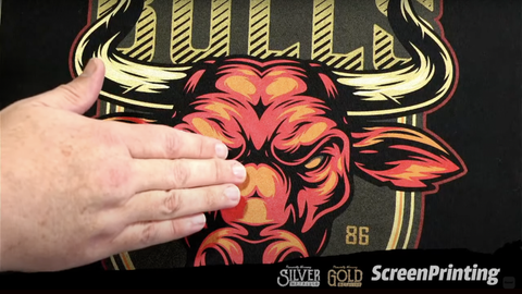 A hand touches a bull design with colored gold ink