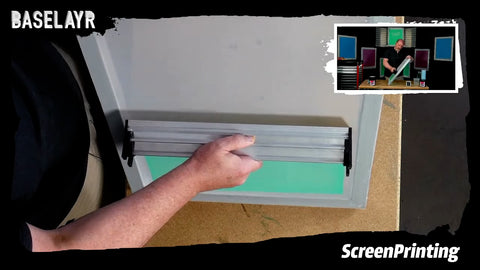 A hand holds a scoop coater to a screen and coats it with green emulsion