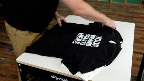 Una mano organiza camisas negras con diseños blancos en una mesa blanca