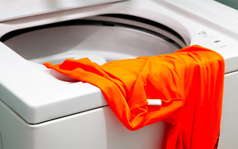 Una camisa naranja tumbada en una lavadora abierta